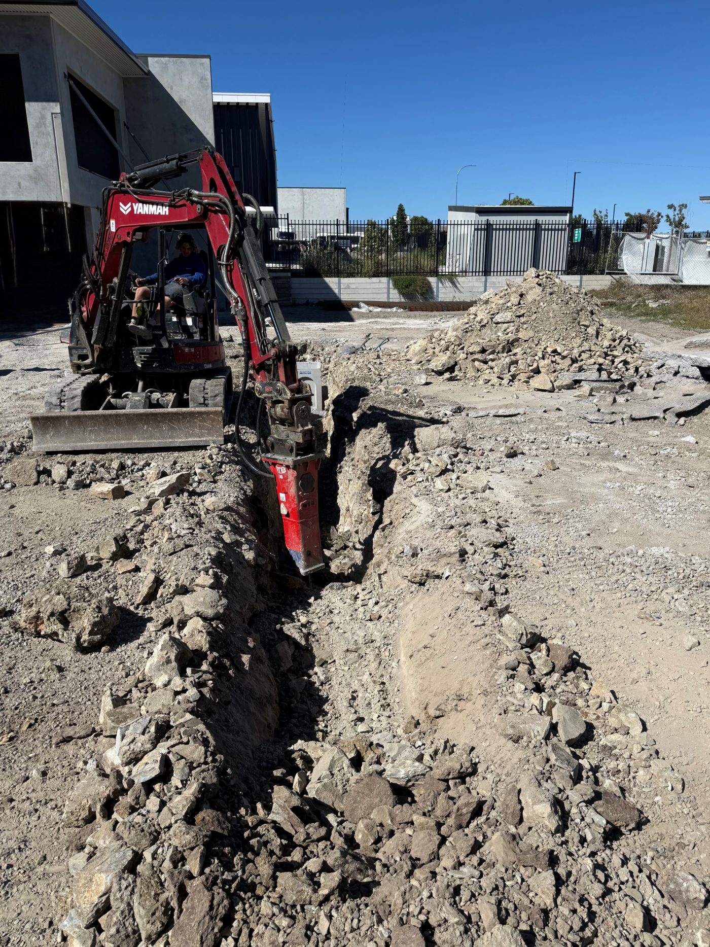 Excavator with rock breaker opening a services trench on a commercial site